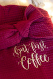 Detail of wine-colored robe featuring "But first, coffee" in latte-colored script text.
