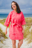 A young woman wears a coral robe on the beach.