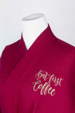 Detail of wine-colored robe featuring "But first, coffee" in latte-colored script text.